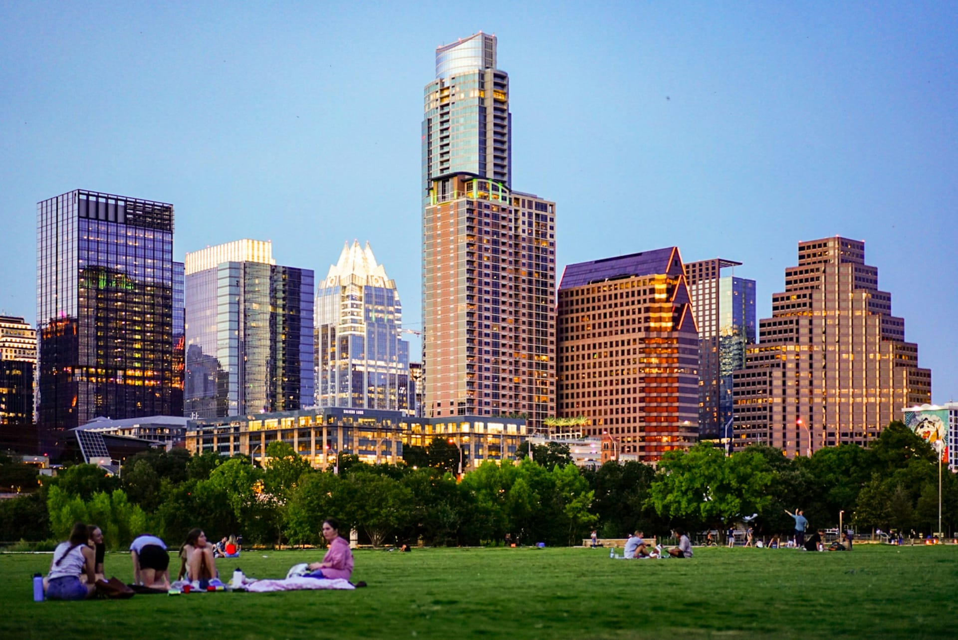 People relaxing on the lawn at Zilker Park with the Austin skyline behind